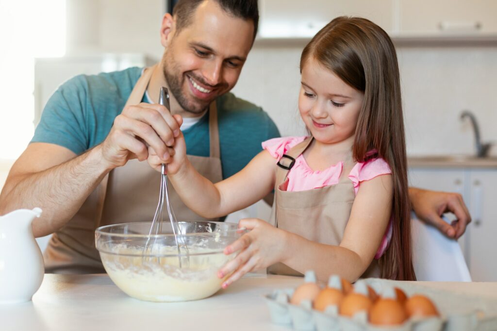 Cheerful Father And Daughter Cooking Pancakes Making Dough In Kitchen