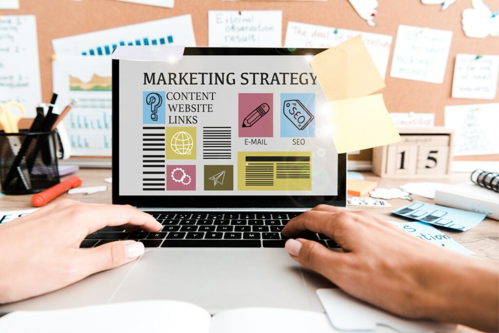 cropped view of woman using laptop with marketing strategy lettering on screen near sticky notes