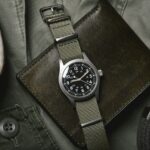 Vintage military watch with nato strap and leather wallet on army green background