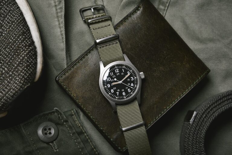 Vintage military watch with nato strap and leather wallet on army green background